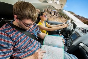 Couple travelling by car in the mountains, woman driving and man is examining the map